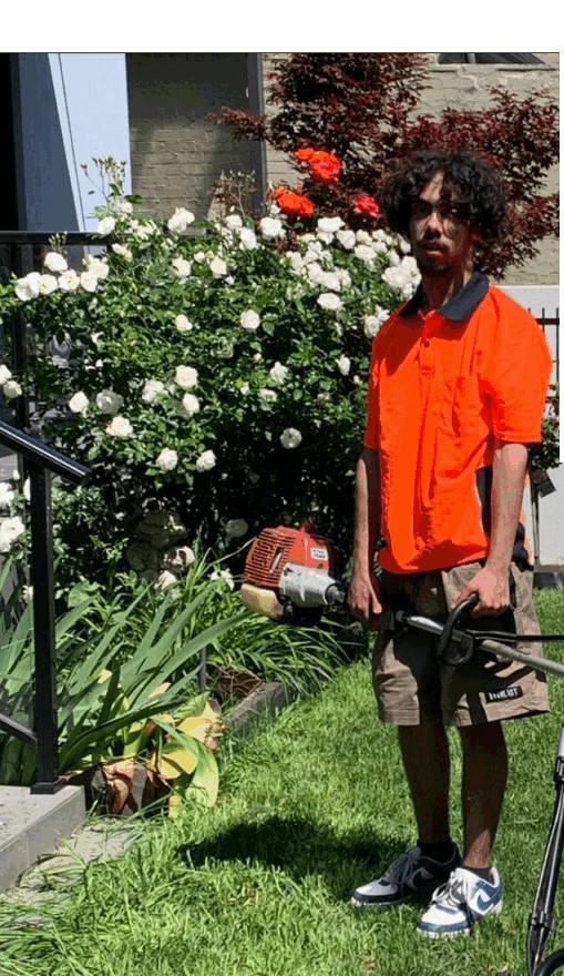 A Lawn Hustlers worker in a hi vis shirt holding a whipper snipper by a rose garden