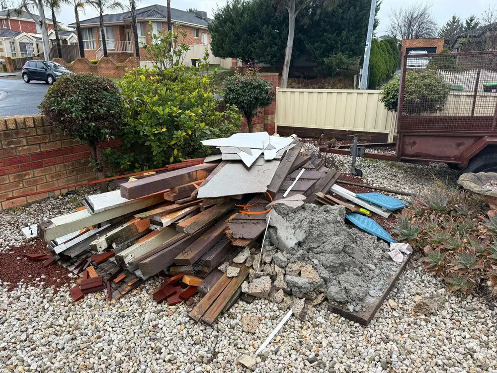 A pile of old timber and broken concrete stacked up in a front garden, ready to load